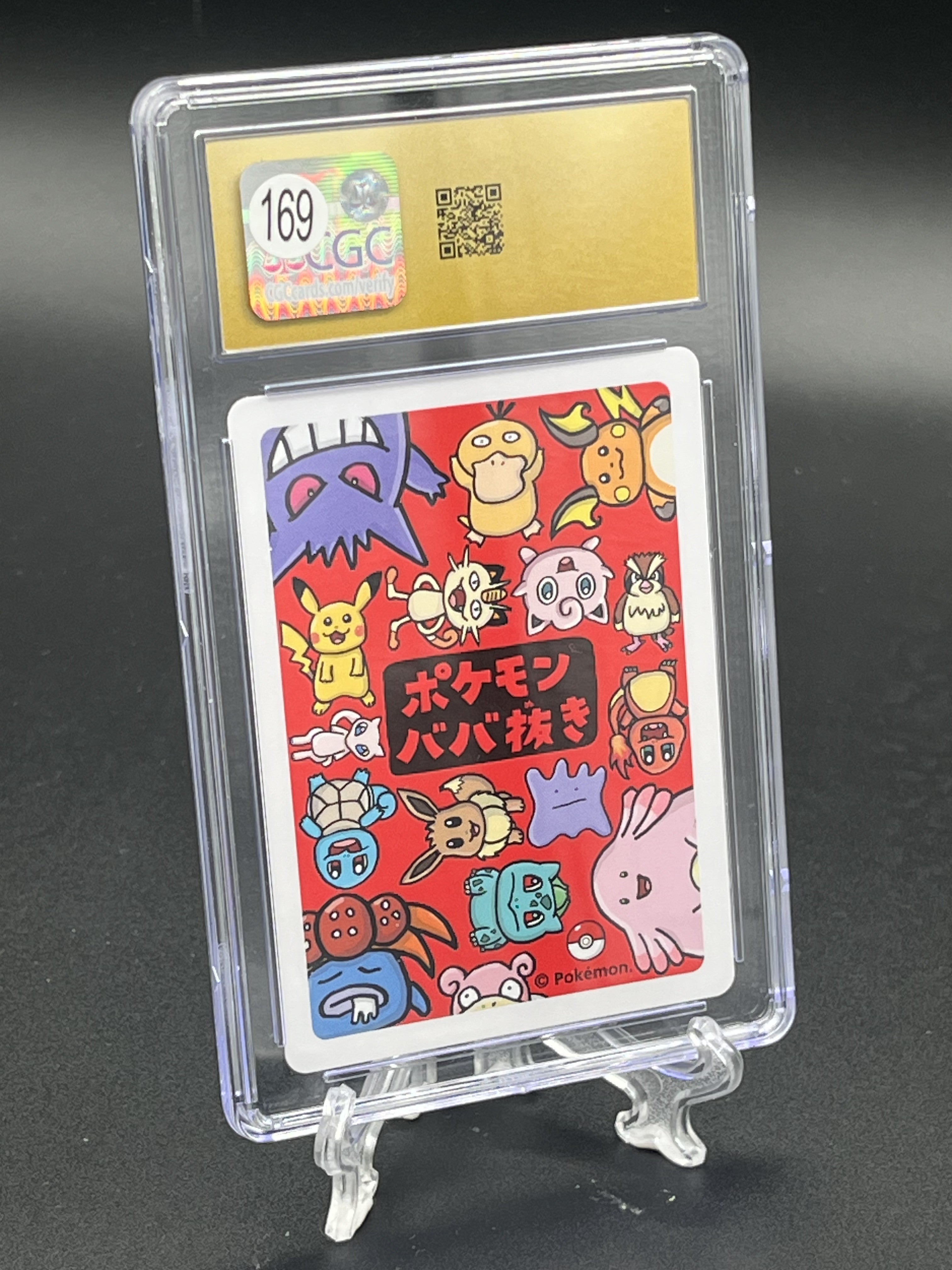 A graded Pokémon card featuring colorful character illustrations on a red background with Japanese text, encapsulated in a clear plastic grading holder and displayed on a small clear stand against a dark studio background.